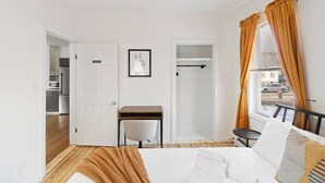 A bedroom with a bed, a desk, and a chair. There is a wardrobe and a window with curtains. - Perfect for Groups! 3BR★Chic & Modern APT near DT! (Providence)