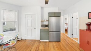 A compact kitchen with a microwave, double-door refrigerator, and a dining area with a table and chairs. - Perfect for Groups! 3BR★Chic & Modern APT near DT! (Providence)