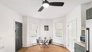 A room with a dining table and chairs, a ceiling fan, and a kitchen area with cabinets and appliances. - Perfect for Groups! 3BR★Chic & Modern APT near DT! (Providence)