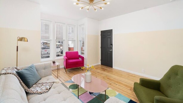 A modern living room with a sofa, a pink armchair, a green armchair, a coffee table, and a unique chandelier. - Perfect for Groups! 3BR★Chic & Modern APT near DT! (Providence)