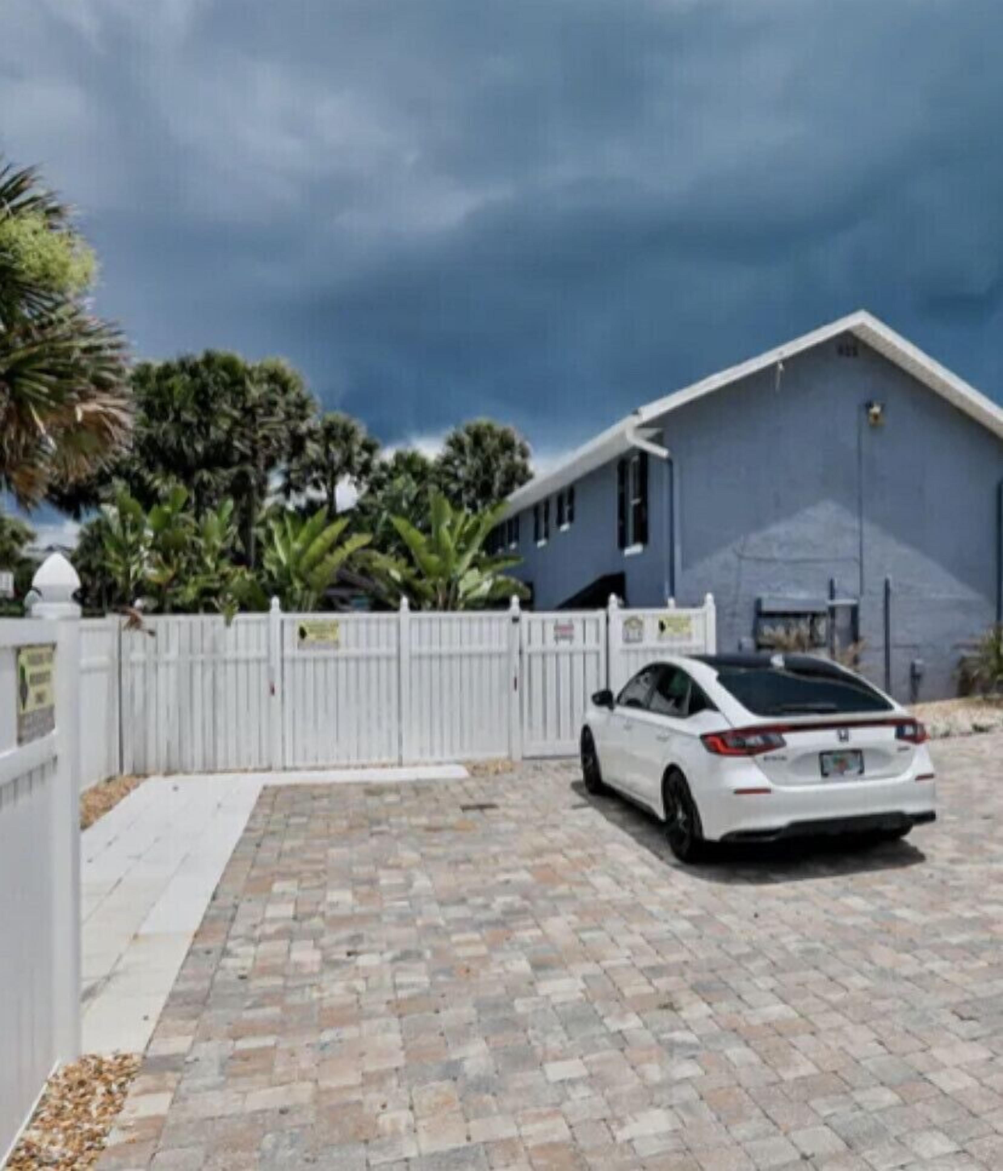 A white car parked in front of a blue house with a white fence.