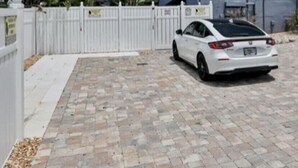 En hvid bil parkeret foran et blåt hus med et hvidt hegn.