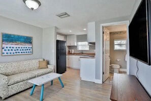 Un espace de vie compact comprenant un canapé, une table basse, un coin cuisine et un téléviseur.