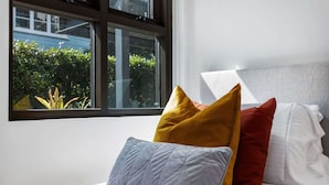 Una cama con almohadas de distintos colores y una ventana con vistas al verdor.
