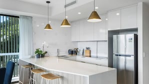 Una cocina moderna con una isla central, electrodomésticos de acero inoxidable, iluminación colgante y taburetes de bar.