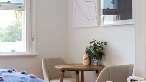 A room with a bed, two chairs, a small round table with a vase of flowers, and a window with blinds. - Intimate Studio Apartment with Balcony in Glebe (Glebe)