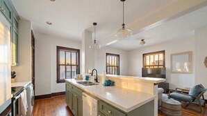 A modern kitchen with wooden flooring, green cabinets, a central island, and pendant lighting. - Charming Historic Loft, 3 Blocks from The Strand (Galveston)