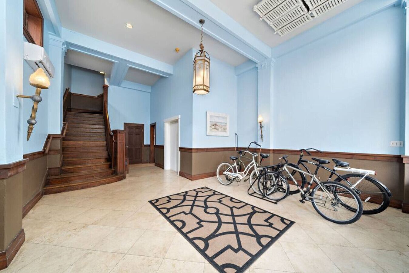 A spacious hallway with a wooden staircase, a patterned rug, and bicycles parked against the wall.