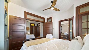 A bedroom with a large bed, wooden doors, a ceiling fan, and a mirror. - Charming Historic Loft, 3 Blocks from The Strand (Galveston)