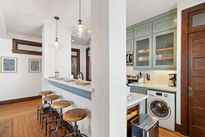 A modern kitchen with a washing machine, bar stools, and a wooden floor.