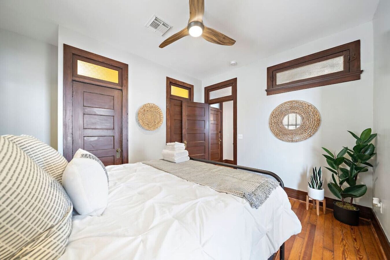 Une chambre à coucher avec un lit, des portes en bois, un ventilateur de plafond et une plante en pot.