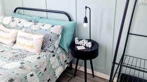A bedroom with a bed, pillows, a bedside table, a lamp, and a radiator.