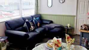 A living room with a black leather sofa, a small round table with floral napkins and plates, and a window with blinds.