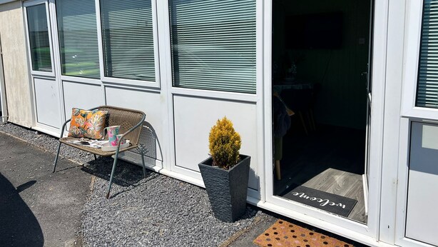 A building with large windows, a door with a mat, a chair, and a potted plant.