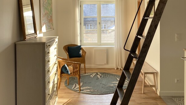 A loft-style room with a wooden ladder, a dresser, a chair, and a window with a view of buildings outside. - Charming mezzanine studio (La Chapelle-Saint-Mesmin)