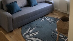 A grey sofa with two blue cushions, a map on the wall, a window with curtains, and a woven basket on a stool. - Charming mezzanine studio (La Chapelle-Saint-Mesmin)