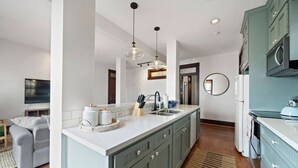 A modern kitchen with a central island, built-in appliances, and a dining area with a sofa and TV. - Stylish Historic Loft, 3 Blocks to The Strand (Galveston)