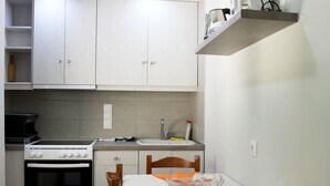 Une cuisine compacte avec des meubles blancs, une cuisinière, un évier et un coin repas comprenant une table et des chaises.