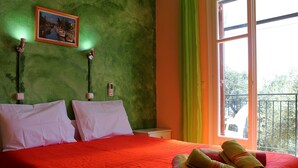 Une chambre d’hôtel avec une couvre-lit rouge, deux oreillers blancs, un tableau encadré au mur et un balcon avec une balustrade.