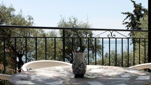 Un balcon avec une table en pierre, un vase décoratif et une vue sur les arbres et l’eau.