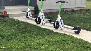 Tre elsparkcyklar står parkerade framför ett modernt tvåvåningshus med en grå fasad och en liten veranda.