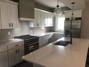 A modern kitchen with white cabinets, a stainless steel refrigerator, a built-in oven, and a large island with a black faucet. - DT Indy near Convention Lucas Oil & Gainbridge Fieldhouse (Indianapolis)