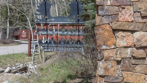 A rustic metal sign with the text "MOOSE GROVE" and "WILSON HOMES" against a stone wall backdrop. - JHRL - Moose Creek #1, Private Hot Tub (Teton Village)