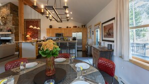 A modern kitchen with wooden cabinets, a central island, and a dining area with a round table set for four. - JHRL - Moose Creek #1, Private Hot Tub (Teton Village)