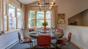 A dining room with a round table, red chairs, a chandelier, and a window with curtains. - JHRL - Moose Creek #1, Private Hot Tub (Teton Village)