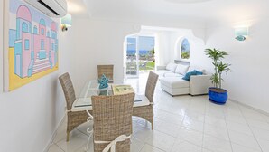 A bright, white interior with a dining area featuring wicker chairs and a glass table, a white sofa with blue cushions, and a potted plant. - Villa dei Lecci Turchese - Luxury private pool villa (Forio)