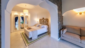 A bedroom with a bed, a sofa, a chandelier, and a stone wall. - Villa dei Lecci Turchese - Luxury private pool villa (Forio)