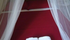 Una cama con una colcha roja y almohadas blancas, cubierta por un dosel blanco.