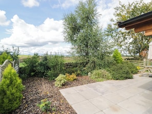 A landscaped garden with a stone wall, various shrubs, and a paved patio area. - Howgills Retreat (Kendal)