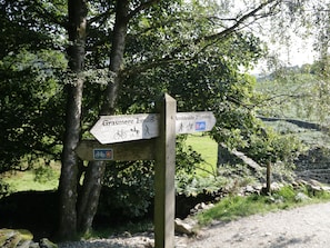 A wooden signpost with directional arrows for Grasmere and Ambleside, indicating distances and accessible modes of transport. - Howgills Retreat (Kendal)