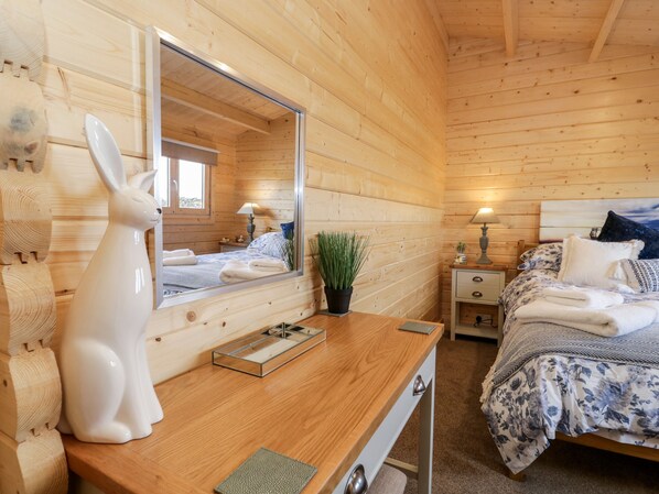 A wooden cabin bedroom with a bed, bedside table, lamp, and a mirror. - Howgills Retreat (Kendal)