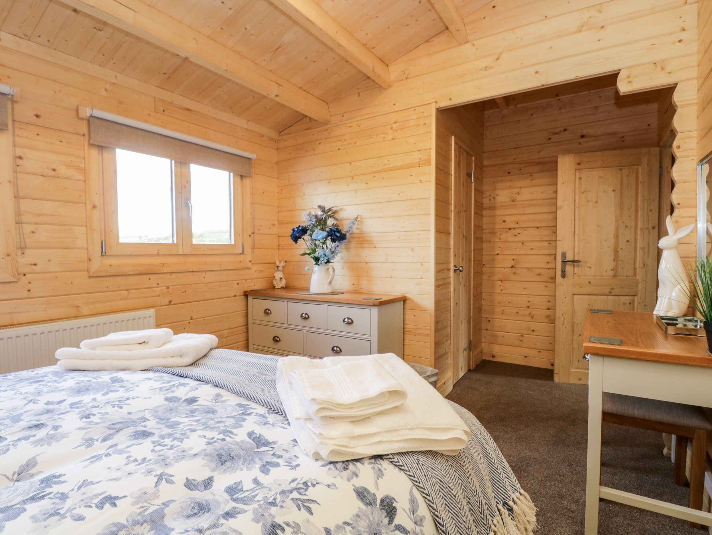 Una habitación de cabaña de madera con una cama, un aparador, una ventana y una puerta.