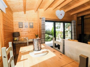 A wooden cabin interior with a dining table, chairs, a heart-shaped decoration, and a view of the outdoors.