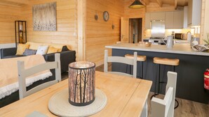 A cozy wooden cabin interior with a dining area, a living room with a sofa, and a kitchen area. - Howgills Retreat (Kendal)