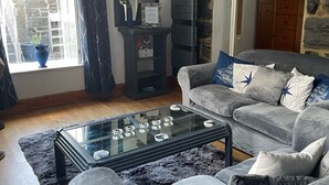 A living room with a grey sofa, a glass coffee table, and a stone wall. - LOVELY 2 BED APARTMENT PORTHMADOG HARBOURSIDE FANTASTIC VIEWS Ffestiniog trains (porthmadog)