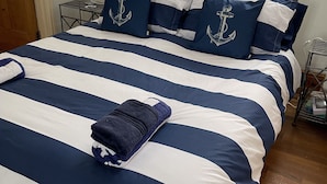 A neatly made bed with navy and white striped bedding, a dark blue throw blanket, and matching pillows with anchor designs. - LOVELY 2 BED APARTMENT PORTHMADOG HARBOURSIDE FANTASTIC VIEWS Ffestiniog trains (porthmadog)