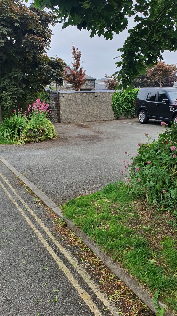 A parking area with a stone wall, a black car, and surrounding greenery. - LOVELY 2 BED APARTMENT PORTHMADOG HARBOURSIDE VIEWS & CLOSE TO FESTINIOGG TRAINS (porthmadog)