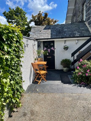 A small, white building with a black door marked '2', a wooden table and chairs, and potted plants. - LOVELY 2 BED APARTMENT PORTHMADOG HARBOURSIDE VIEWS & CLOSE TO FESTINIOGG TRAINS (porthmadog)
