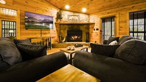 A cozy log cabin interior with a fireplace, comfortable seating, and a large painting of a mountain landscape. - Family Friendly ~ Large Deck ~ Hot Tub ~ Game Room ~ Secluded Getaway (Sevierville)