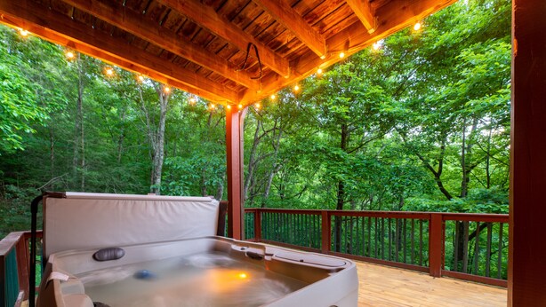 A hot tub on a wooden deck surrounded by trees, with string lights above. - Family Friendly ~ Large Deck ~ Hot Tub ~ Game Room ~ Secluded Getaway (Sevierville)