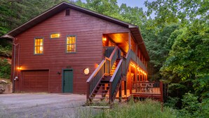 A wooden cabin with a green door, a staircase, and a porch with string lights. - Family Friendly ~ Large Deck ~ Hot Tub ~ Game Room ~ Secluded Getaway (Sevierville)