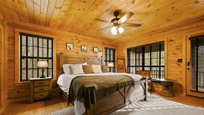 A wooden cabin bedroom with a bed, nightstands, a table, and a ceiling fan. - Family Friendly ~ Large Deck ~ Hot Tub ~ Game Room ~ Secluded Getaway (Sevierville)