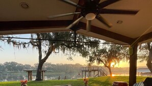 Un patio exterior con un hogar a leña de ladrillo, asientos y vistas a un lago al atardecer.
