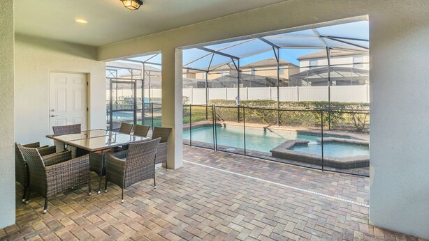 Eine Außenpatio mit einem Glastisch und Stühlen, einem Backsteinboden und Blick auf einen Swimmingpool und Nachbarhäuser.