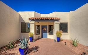A house with a tiled roof entrance, a blue door, and potted plants.