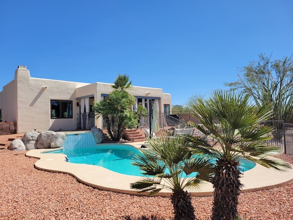 A modern house with a swimming pool, surrounded by pebbles and palm trees.